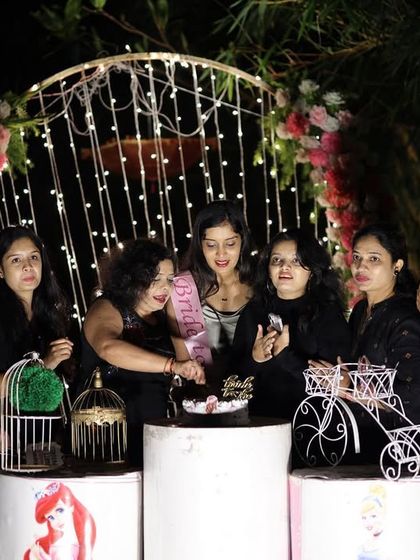 A "Bride to be" party with a charming outdoor setup. The decor includes a floral arch with fairy lights and whimsical props like a miniature bicycle and birdcages.