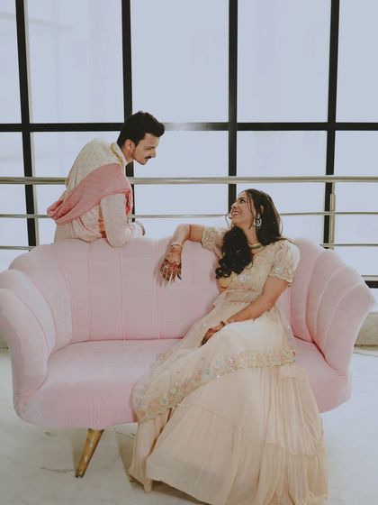 A full-length view of the couple on the pink sofa, showcasing their outfits and the stylish setup.