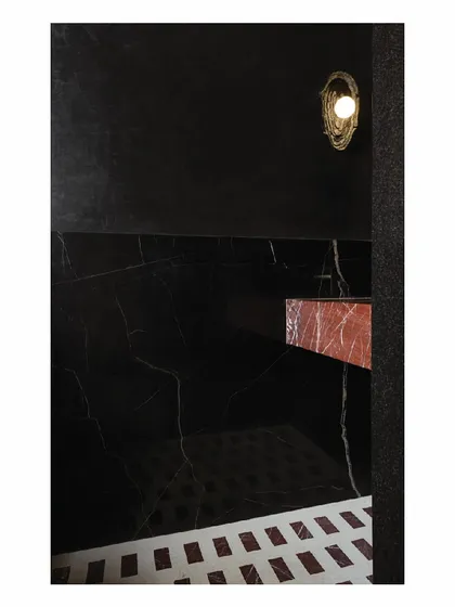 A wider view of the dramatic powder toilet, showing how the in-situ red and white marble floor pattern connects with the monolith red marble basin. The entire room is a composition of bold materials and dark tones, designed to be an immersive and memorable space for guests.