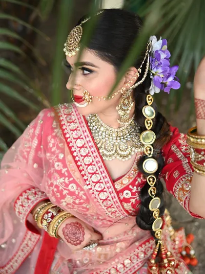 A side profile of a model in our red and pink lehenga, showing off her intricate hairstyle with floral and mirror accessories, which we can help you find inspiration for.