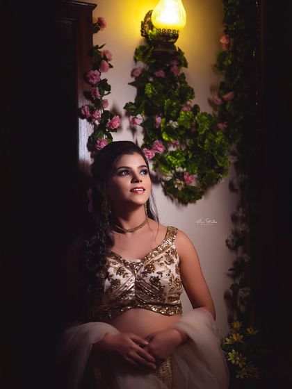 An artistic portrait of a bride in a white and gold lehenga, looking up towards the light. The dramatic shadows create a dreamy and contemplative mood.