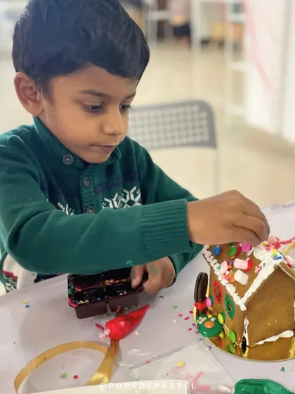 This young boy is completely absorbed in decorating his gingerbread house with an assortment of colorful candies.