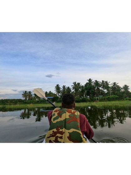 A kayaker paddles along the green edge of the lake, surrounded by nature.