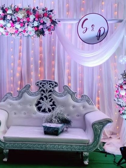 A view of the pink and white engagement stage, showing the draped monogram and the side floral arrangement. The soft lighting creates a romantic and gentle ambiance.
