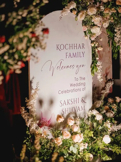 A classic and elegant welcome sign for Sakshi and Shuvam's wedding celebration, nestled within a bed of beautiful pastel roses.