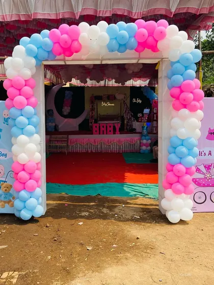 The entrance to a baby shower with a pink, blue, and white balloon arch and gender-themed banners.