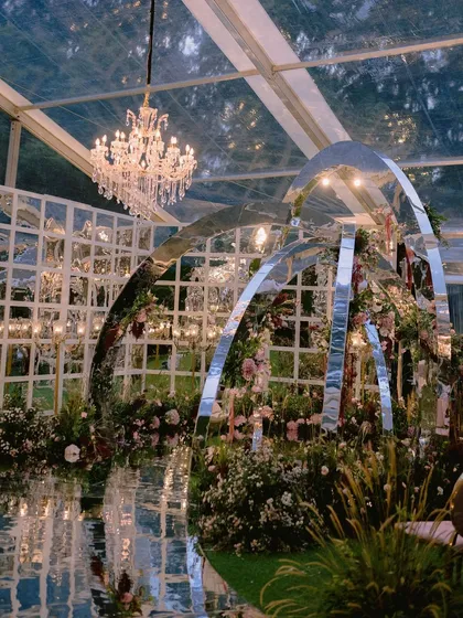 We dreamt up this one-of-a-kind contemporary mandap for Nidhi and Amit, featuring mirrored arches that reflected the lush floral gardens we created inside a clear marquee. It was a modern fairytale, built to reflect their unique personalities, even amidst a cyclone in Bangalore.