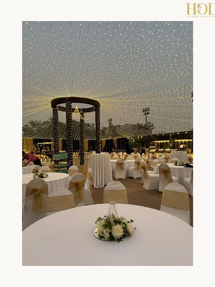 A closer view of the fairy light canopy over the dining tables, showcasing the elegant white and gold chair covers and simple floral centerpieces.