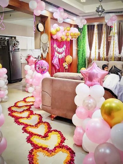 A full living room decoration for a baby girl's welcome. The setup includes a pathway of hearts made from flower petals, balloon pillars, and a decorated backdrop, transforming the entire space.