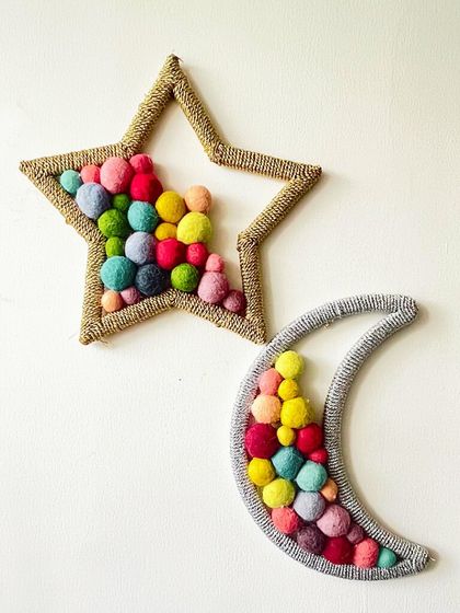 These star and moon wall hangings are filled with colorful pom-poms, making them a playful and whimsical addition to a nursery or kid's room. They can be hung as a pair or separately to sprinkle a little magic on the walls.