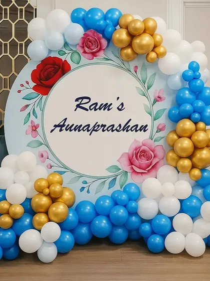 We design elegant and personalized backdrops for traditional ceremonies like this Annaprashan. The setup features a custom circular backdrop with the baby's name and event, framed by a beautiful balloon arrangement in blue, white, and gold.