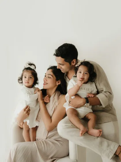 A classic family portrait with parents and their two daughters. The coordinated neutral outfits and simple background keep the focus on their connection.