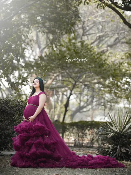 A serene portrait of a mother-to-be in a wine-colored ruffled gown, enjoying a quiet moment in a park-like setting.