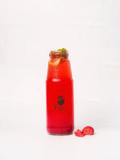 A vibrant red strawberry mojito or cooler in a glass bottle, with fresh strawberry pieces nearby. The white background makes the drink's color pop, creating a refreshing image.