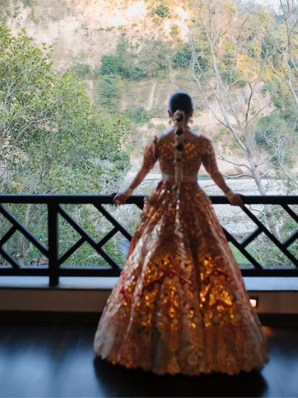 A back-shot of a bride in her shimmering lehenga, looking out at the scenic view from her balcony.