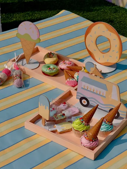 A playful spread for an ice cream-themed birthday party. The setup includes cupcake cones, donuts, and custom wooden cutouts of ice cream trucks and cones.