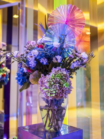 A single vase of flowers with iridescent accents set against the colorful entrance tunnel. This shot highlights the interplay of natural beauty and modern materials.