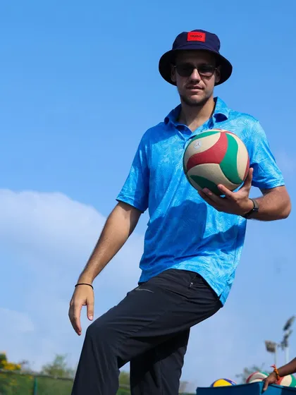 I hold the ball to demonstrate the correct height and position for a player to practice their serve. Hands-on coaching ensures every detail is perfected.