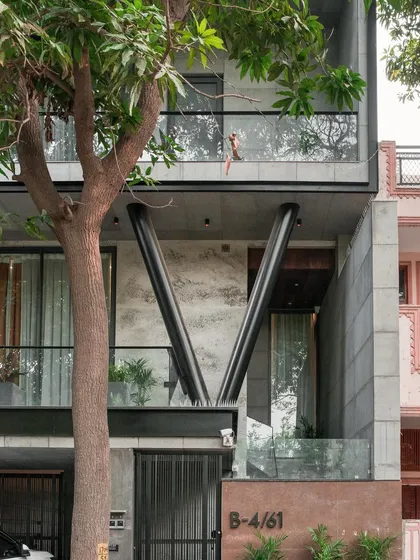 A daytime detail of the Paschim Vihar residence. The angled steel columns provide structural support while acting as a powerful design element, contrasting with the raw concrete and glass.