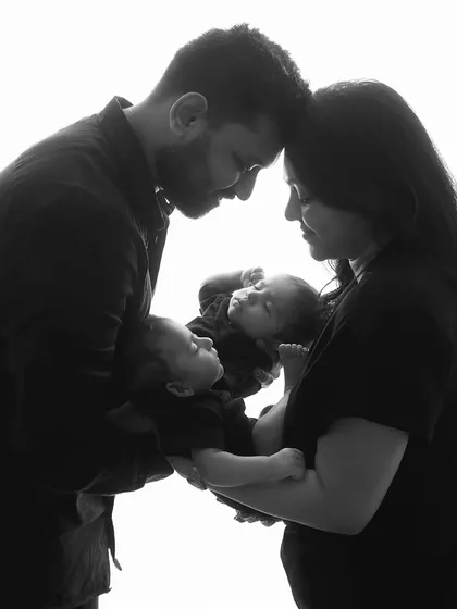 An intimate black and white portrait of the parents holding their twins, their heads touching. This pose is full of love, connection, and the magic of having two new babies.