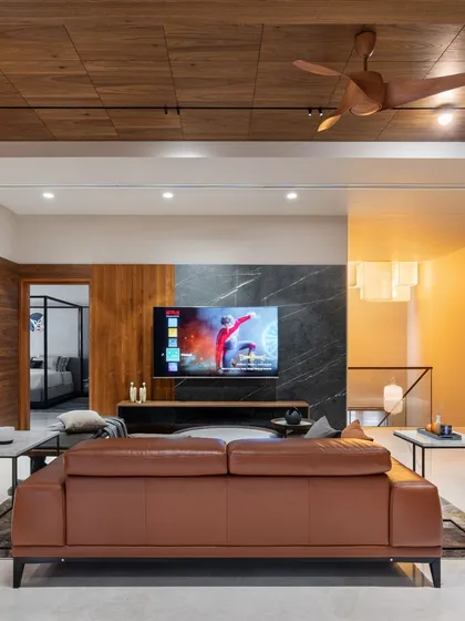 This view shows the family living area, with a comfortable leather sofa facing a media wall that features a stunning black marble panel. The wooden ceiling and track lighting continue the home's cohesive design language.