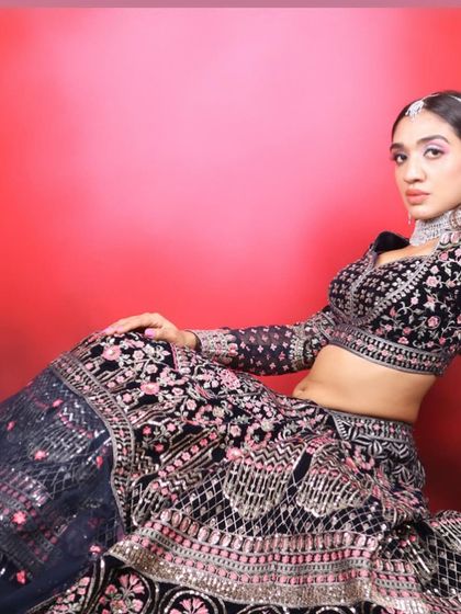 A full-length seated pose, showing the beautiful silhouette of the lehenga and the confident attitude of the makeup.