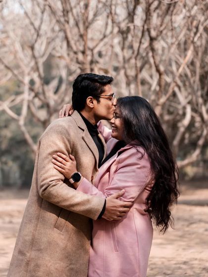 A warm embrace in a winter forest. The matching coats and the gentle forehead kiss create a cozy and romantic image.