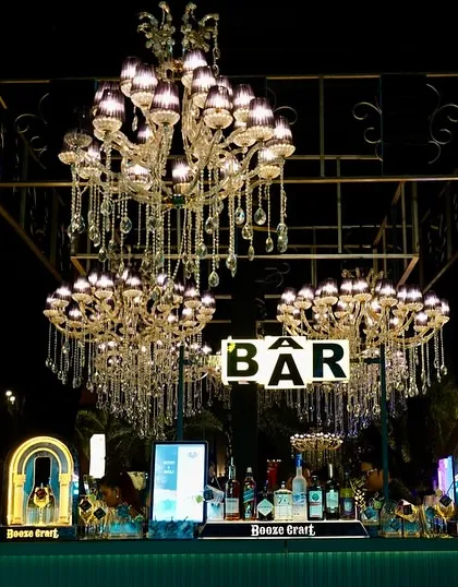A stunning bar setup for a 25th-anniversary cocktail party, featuring a canopy of crystal chandeliers. This opulent design makes the bar a central and glamorous feature of the event.