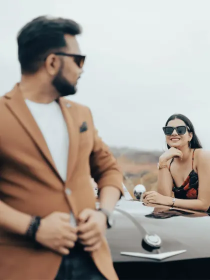 A stylish shot of the couple with a vintage car. The groom is out of focus in the foreground, drawing attention to the bride's happy expression.