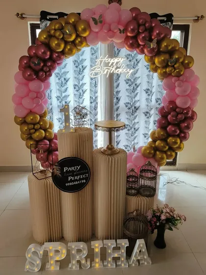 A glamorous first birthday balloon ring in shades of metallic pink and gold, with a 'Happy Birthday' neon sign and the child's name in light-up letters.