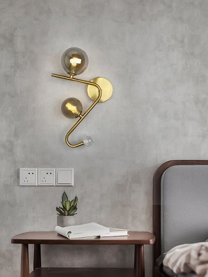 A modern, minimalist wall sconce with a zig-zagging arm and two smoked glass globes. A perfect bedside lighting solution.