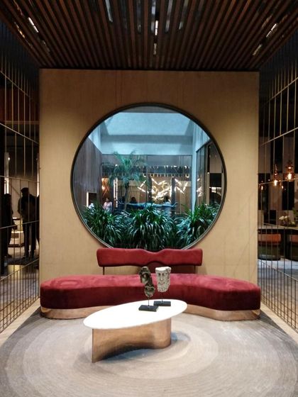A dramatic, custom-curved sofa in a rich red velvet creates an intimate seating nook. The piece is designed to complement the architectural circular window, which looks out onto a lush green courtyard.
