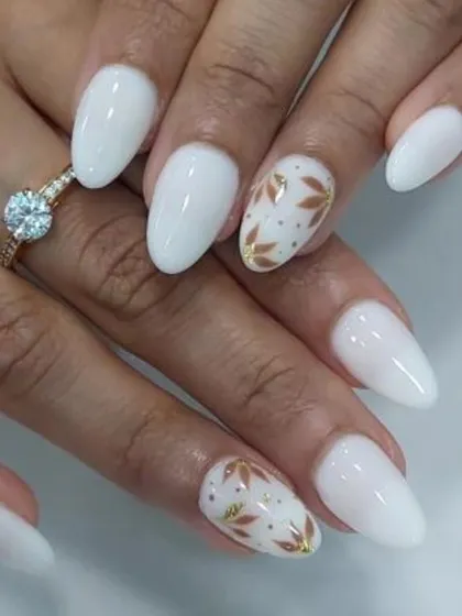 A clean and classic bridal look. This design features milky white almond-shaped nails with two accent nails showcasing delicate, hand-painted gold leaf patterns.