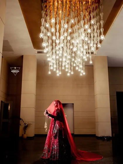 A dramatic silhouette of the bride holding her veil, standing under a magnificent modern chandelier. This shot is all about creating a grand and artistic bridal portrait.