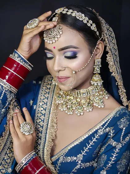 A royal blue bridal ensemble paired with heavy kundan jewelry. The makeup features a dramatic purple and blue cut-crease, showcasing advanced eye makeup techniques.