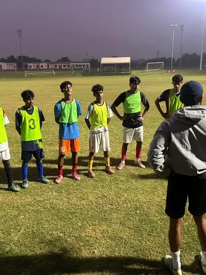 A coach addresses his team under the lights. We train players to be tactically flexible and mentally prepared for any game situation.