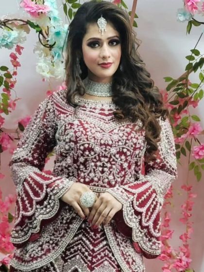 A full view of the modern maroon gown with bell sleeves and intricate embroidery, set against a floral backdrop.