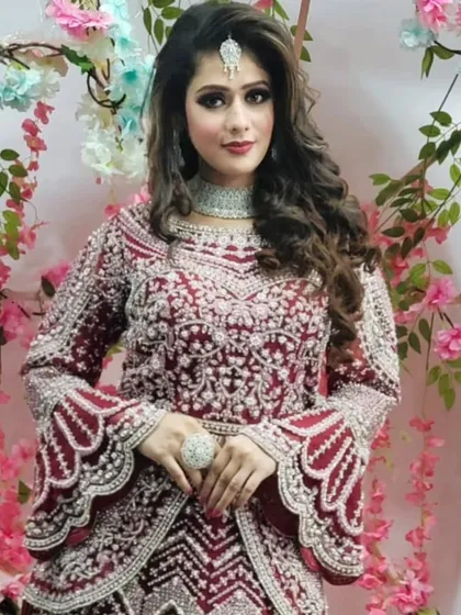 A full view of the modern maroon gown with bell sleeves and intricate embroidery, set against a floral backdrop.