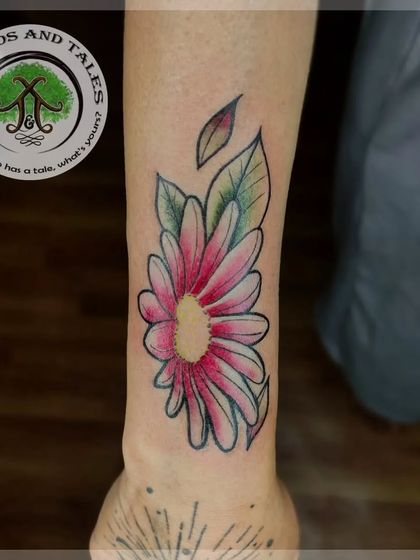 A custom daisy flower tattoo with a watercolor effect. The pink and white petals are blended with green leaves for a fresh, artistic look.