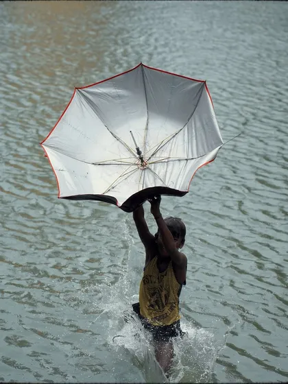 A child emerges from the water, holding an inverted umbrella that has caught the water and the light. It's a unique and joyful image that captures the playful spirit of the monsoon.