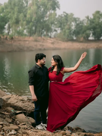 The wind catches her red dress, creating a beautiful, dynamic shape. This shot combines a sense of drama and romance, highlighting the couple against the lakeside scenery.