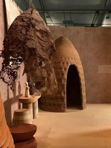 A view of the 'Soil' installation featuring a hanging, nest-like sculpture and a small, hut-like structure. These forms evoke a sense of primitive shelter and connection to the earth.