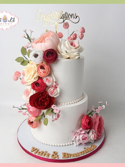 A cascade of florals for a beautiful celebration. This two-tiered white cake is adorned with a waterfall of handcrafted sugar flowers in shades of red, pink, and peach.