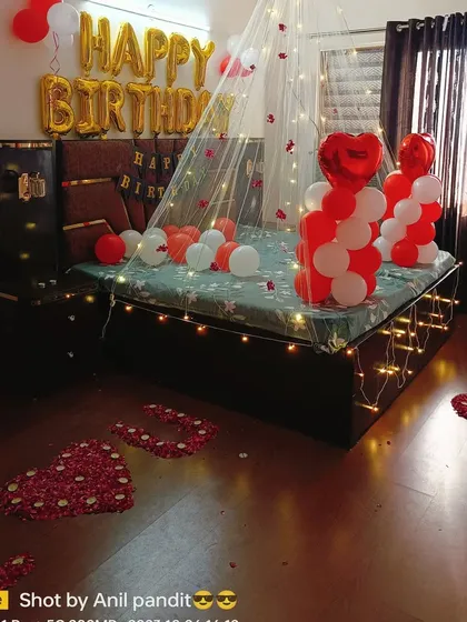 This is a complete birthday bedroom makeover. It features a lighted canopy, "HAPPY BIRTHDAY" foil balloons, and a personal touch with "I LOVE YOU" spelled out on the floor using rose petals.
