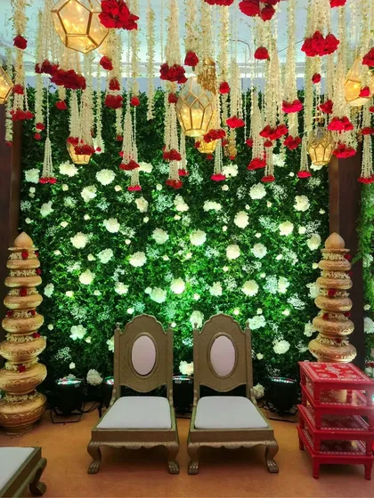 This mandap setup features a stunning backdrop of a green floral wall with hanging jasmine and red rose garlands, creating a vibrant and traditional look.