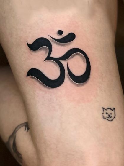 A bold and 3D-style Om tattoo. The shading is done in a way that makes the symbol appear raised from the skin, giving it a unique and modern look.