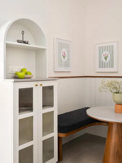 This cozy breakfast nook in the 'Palaash' project features a custom-built bench and a freestanding arched crockery unit, creating a charming spot for quick bites.