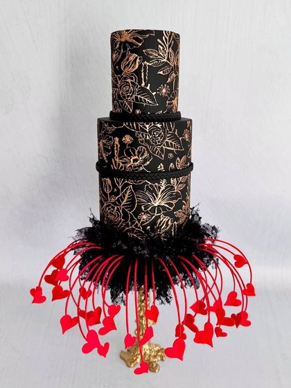 The full view of my "Eclipsed Romance" concept cake. The three tiers are covered in black fondant with hand-painted gold flowers, and the base is a dramatic explosion of red sugar hearts.
