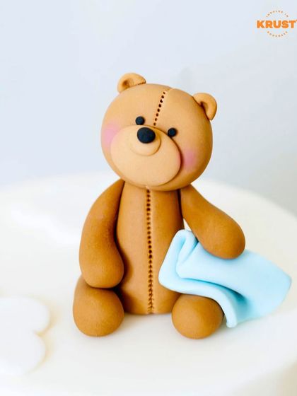 A beautifully crafted fondant teddy bear sitting on a cake. This is a great example of the cake decorating skills you can learn with us.