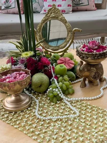 A close-up of a 'Bagh-e-Ishq' themed tablescape, blending fresh fruits, delicate flowers, pearls, and traditional brass decor. Our traditional event designs are rich with poetic details and cultural heritage.